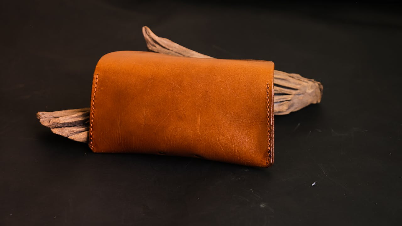 who-we-are Elegant brown leather wallet displayed on a rustic wooden piece with a black studio backdrop.