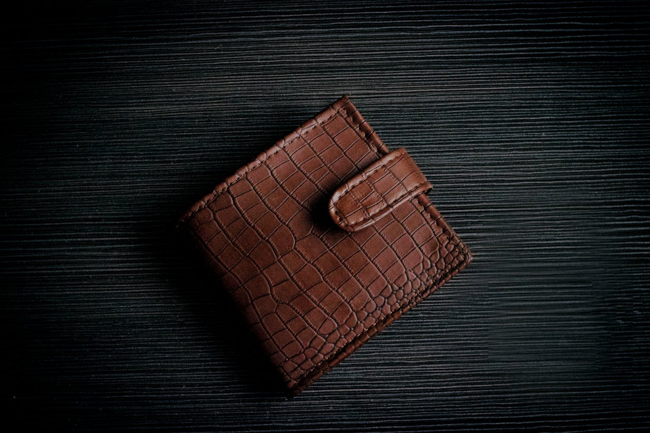 A stylish brown leather wallet with a textured design lies on a dark surface, showcasing its elegant craftsmanship.
