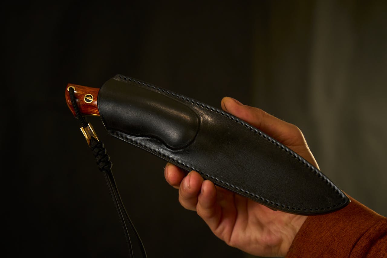 about-bg Close-up of a handmade knife with a leather sheath held by an adult hand.