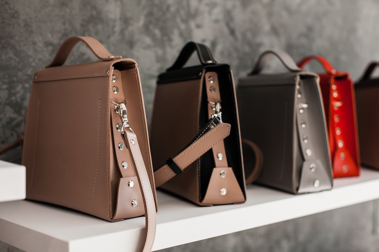 our-story Luxury leather handbags displayed on a white shelf, showcasing minimalistic design and various colors.